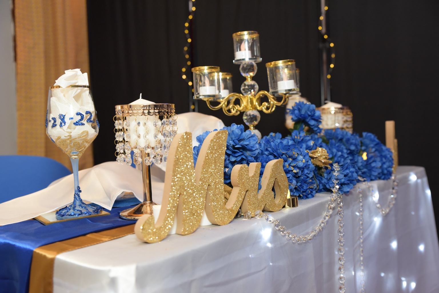 Blue flowers, gold candles, and a Mrs sign at the wedding sweetheart table