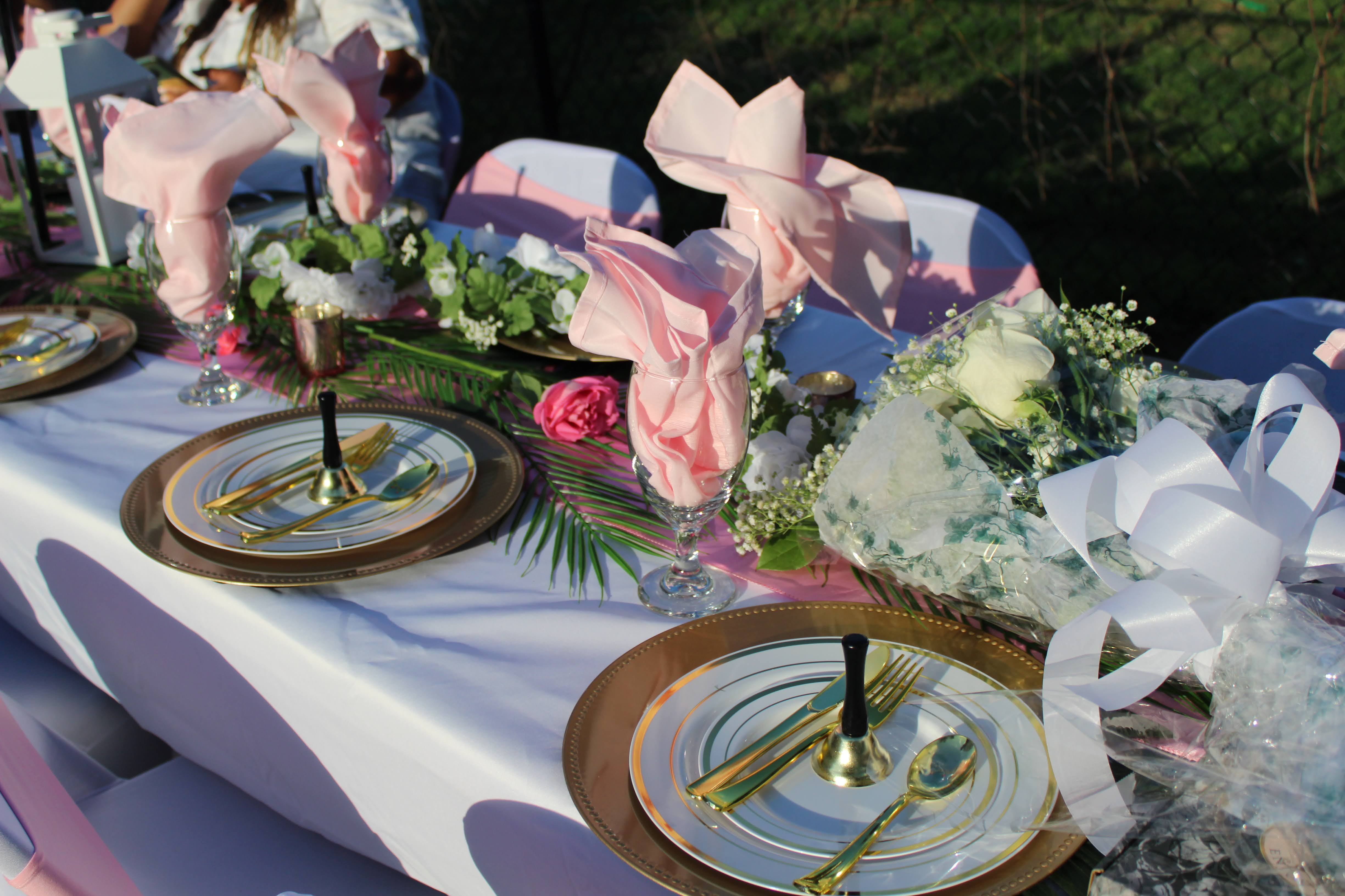 Pink napkins, white flowers, and gold place settings at an outdoor wedding reception